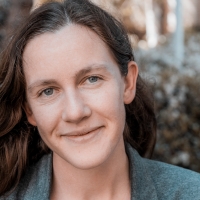 Close-up headshot of Danica Loucks wearing a gray blazer; they have long brown hair and gray-blue eyes and are smiling.